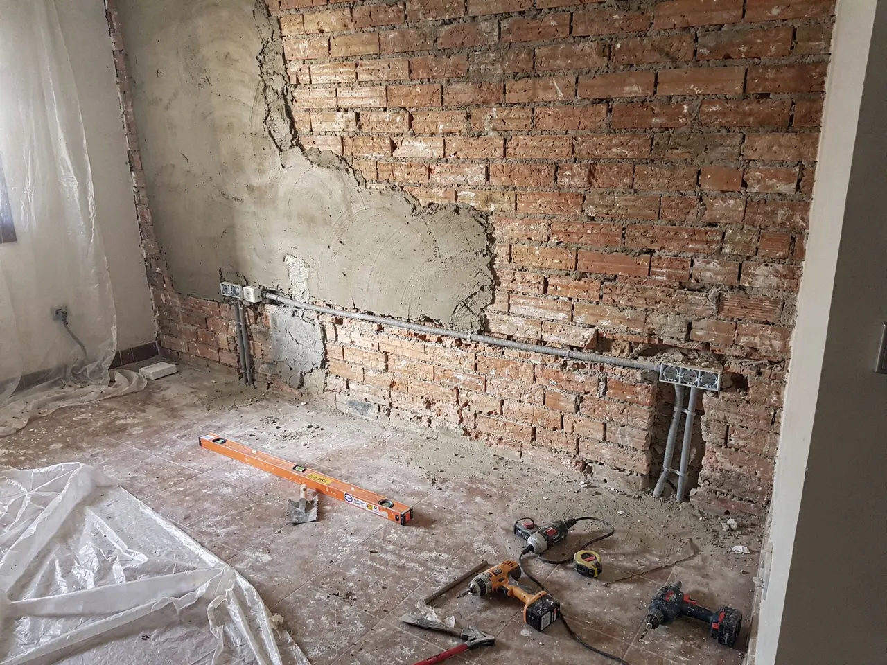Obra en marcha: pared de ladrillo visto con las instalaciones nuevas y herramientas