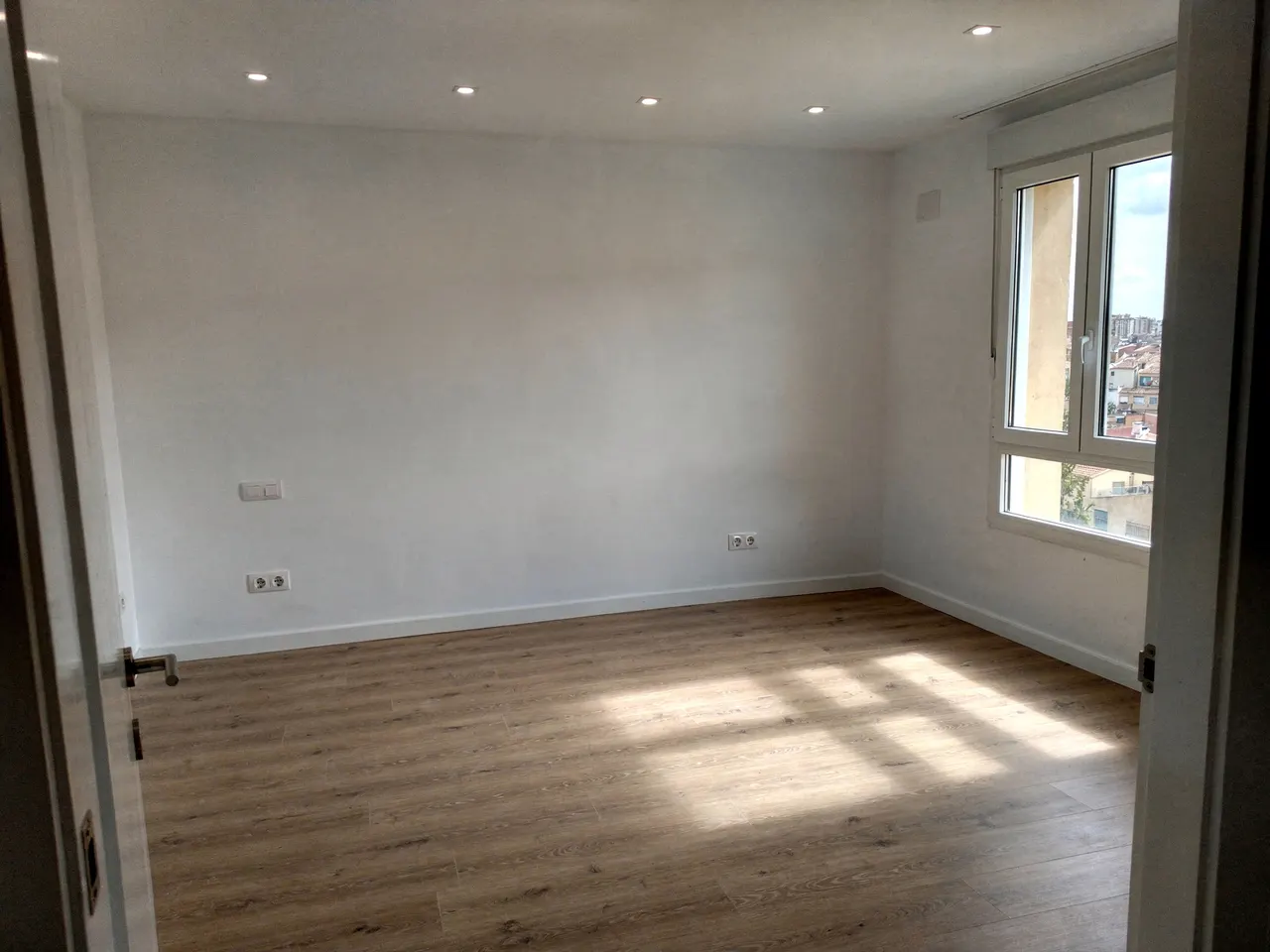 Salón reformado con suelo laminado, focos en el techo y ventana con vistas a Valladolid