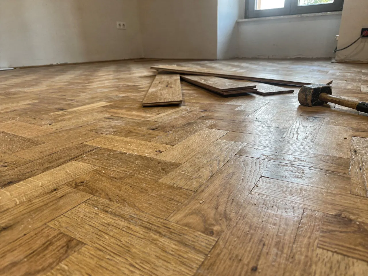 Parquet en espiga a medio colocar, con las tablas y la maza sobre el suelo